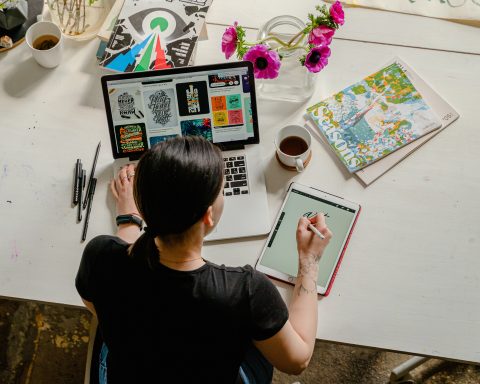 Woman writing on a tablet while using her laptop.